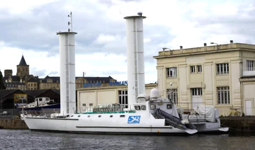 Bateau avec grands mâts amarré près d'un bâtiment.